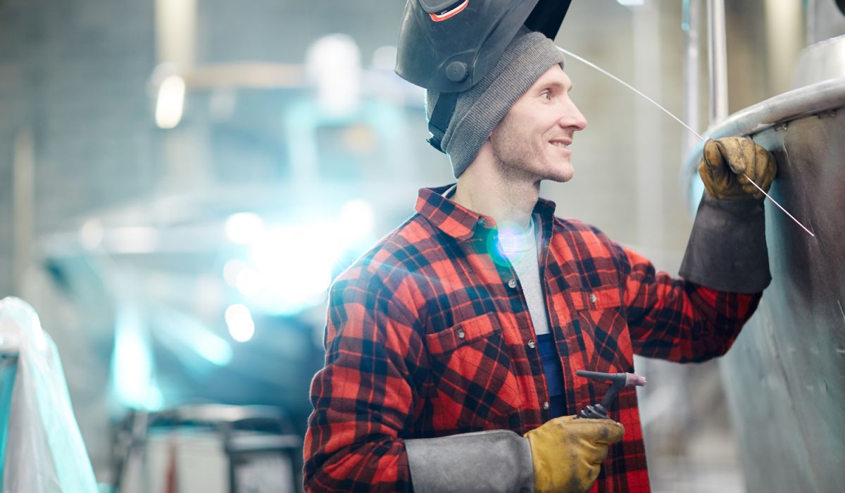 Manlig svetsare arbetar med aluminiumbåt i en industrihall
