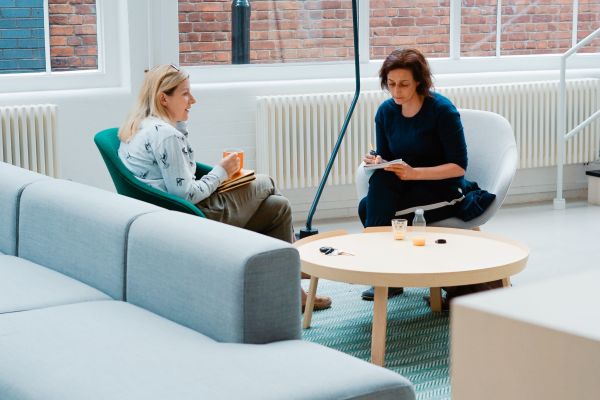 Personer som sitter och diskutterar vid en blå soffa.