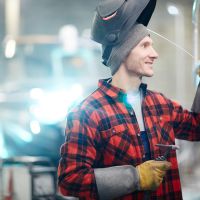 Manlig svetsare arbetar med aluminiumbåt i en industrihall