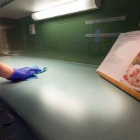 En hand med blå skyddshandske torkar av ett bord